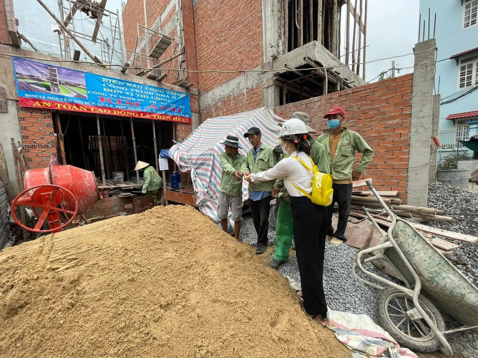 Công nhân đang xếp gọn các bao cát và xi măng vào một góc nhỏ trong công trình, chừa lối đi thông thoáng.